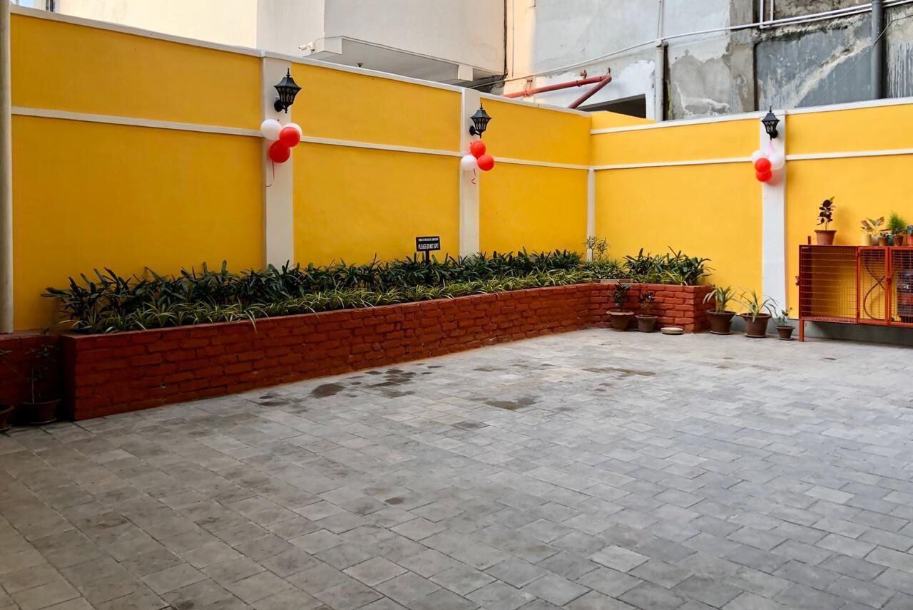 Une cour avec des murs jaunes, des ballons rouges et blancs, et des plantes en pot.