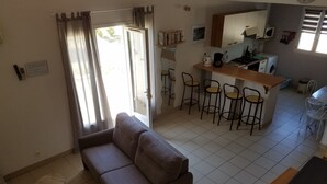 A compact living space with a sofa, a small dining table, and a kitchenette area. - Gîtes du Combeau (Saint-Maurice-d'Ibie)
