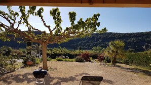 A covered outdoor area with a barbecue grill, a folding chair, and a table. - Gîtes du Combeau (Saint-Maurice-d'Ibie)