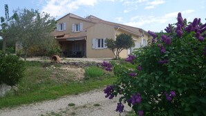 A house with a gravel driveway, a garden with purple flowers, and a stone wall. - Gîtes du Combeau (Saint-Maurice-d'Ibie)