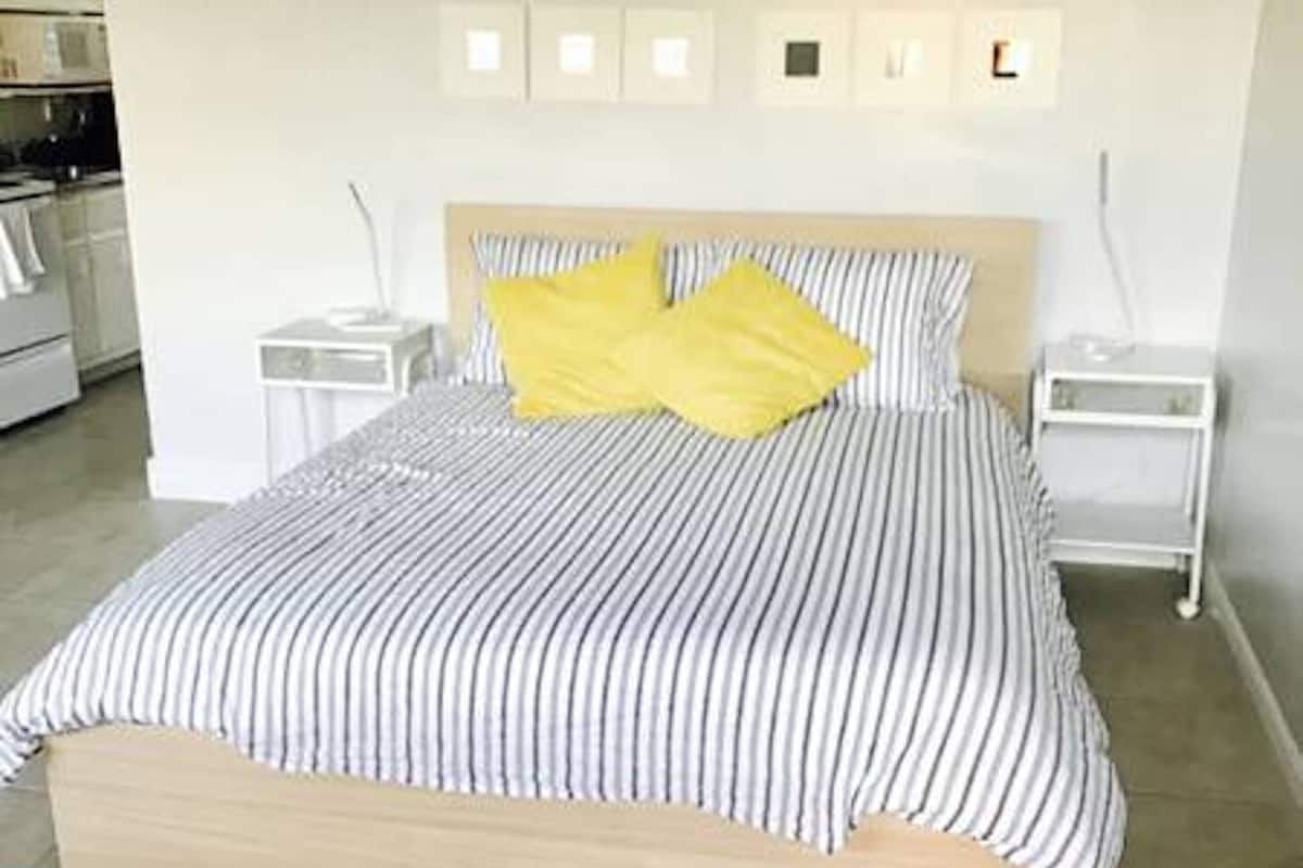 A bedroom with a bed, two bedside tables, a nightstand, and a wall-mounted light fixture.