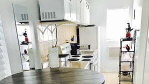A modern kitchen with white cabinets, a stove, and a sink. There is a round table with two black stools. - Petrina Studio Apartment (Pompano Beach)