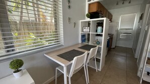 A compact kitchen with a dining area, featuring a small table, two chairs, a white cabinet with a 'Wi-Fi' sign, and a potted plant. - Petrina Studio Apartment (Pompano Beach)