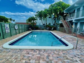 A rectangular pool with a tiled edge, surrounded by a brick patio. - Petrina Studio Apartment (Pompano Beach)