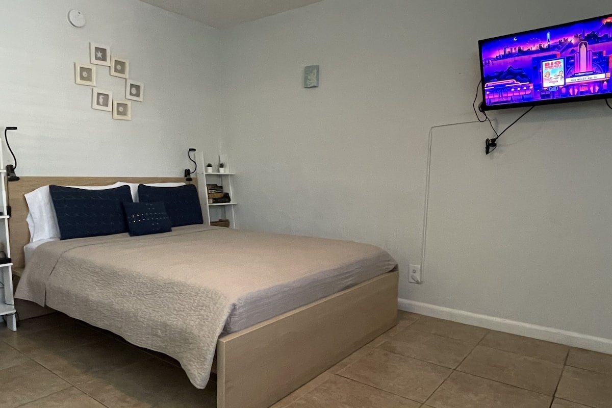 A bedroom with a bed, a TV mounted on the wall, and a shelf with decorative items.