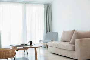Una sala de estar moderna con un sofá beige, una mesa redonda de madera con un libro y una taza, y una silla de mimbre.