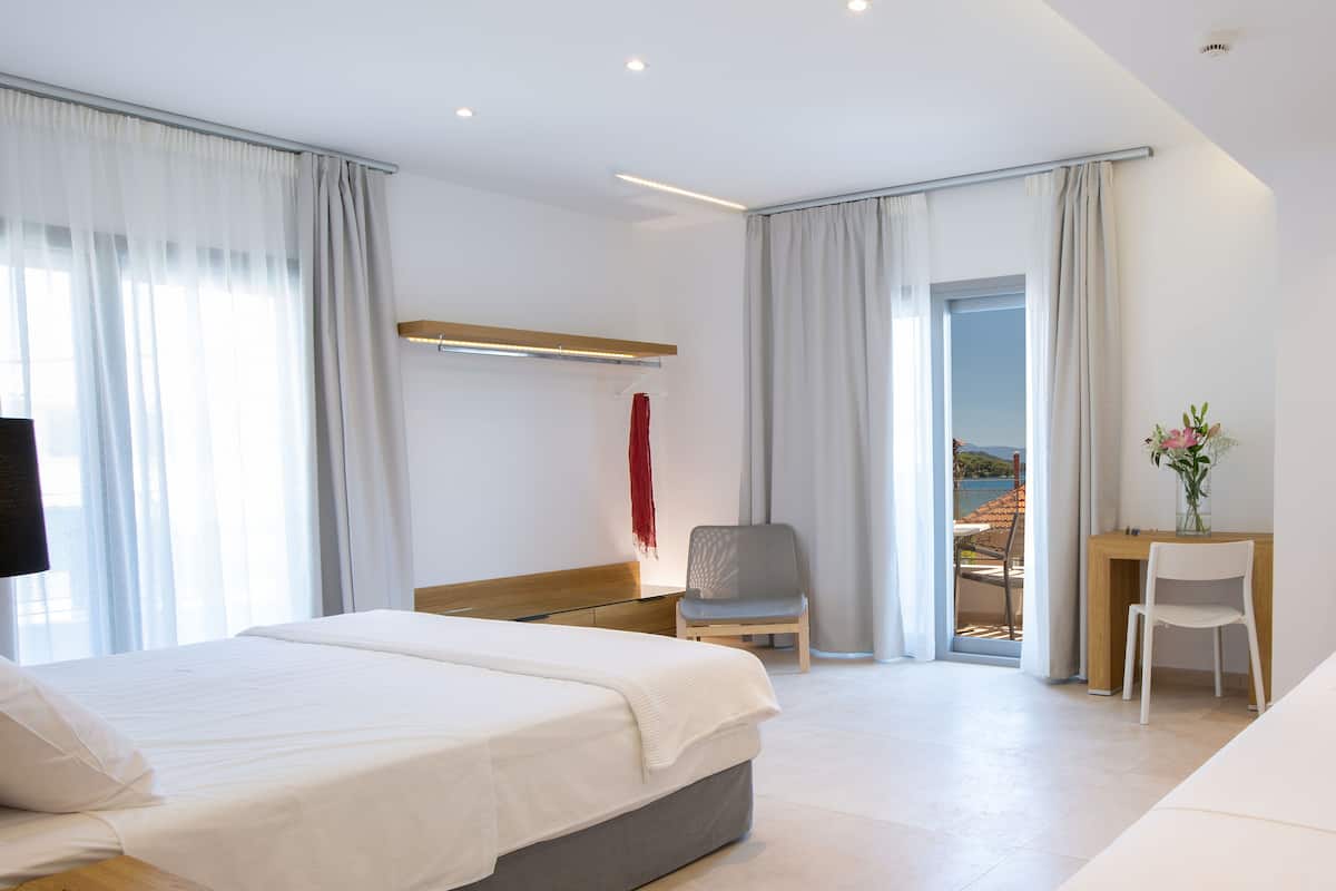 A modern hotel room with a large bed, a desk, a chair, and a view of the outdoors.
