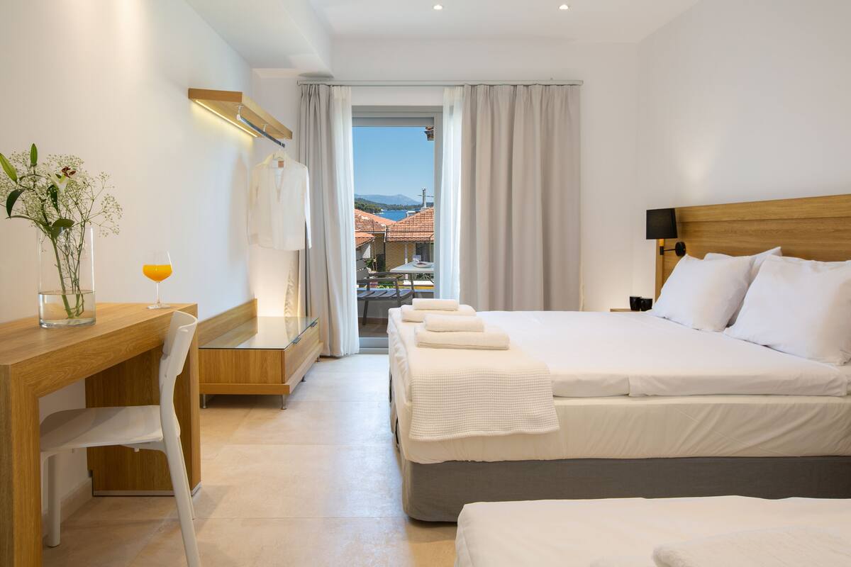 A hotel room with a bed, a desk, and a chair. There is a view of buildings and mountains outside the window.
