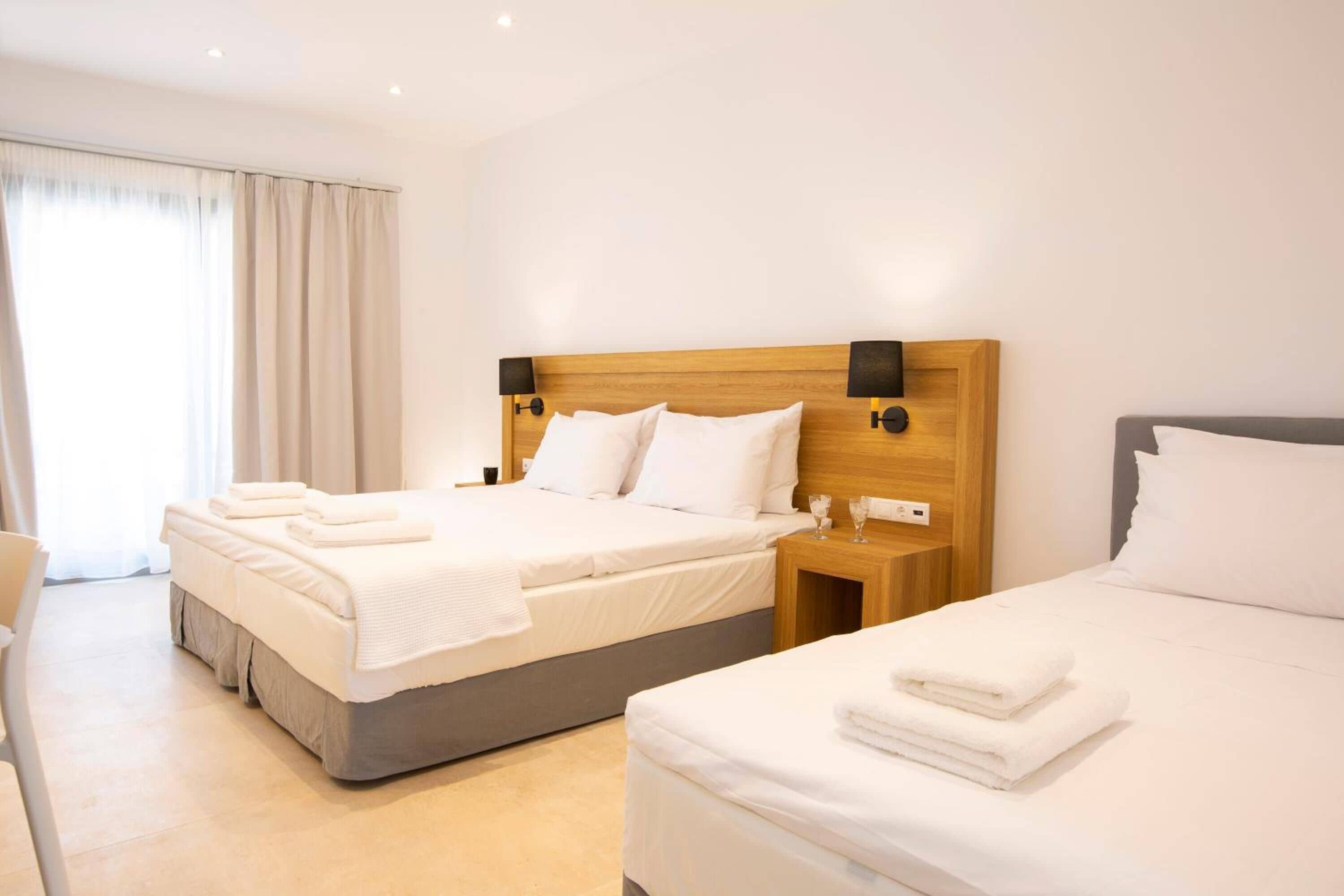 Une chambre d’hôtel avec deux lits, une tête de lit en bois, du linge de lit blanc et une table de chevet avec un verre.