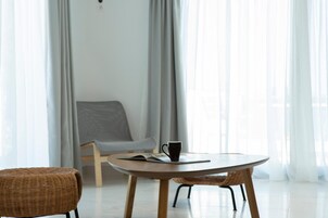 Una habitación moderna y minimalista con una mesa redonda de madera, una silla de mimbre y un sillón gris.
