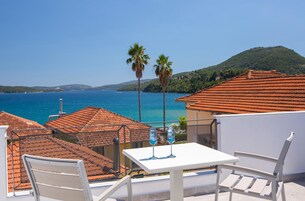 Una terraza con una mesa y sillas blancas, con vistas a la costa, tejados rojos y palmeras.