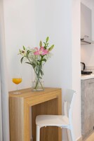 Una habitación moderna con una mesa consola de madera, una silla blanca, un florero con flores y un vaso de jugo de naranja.