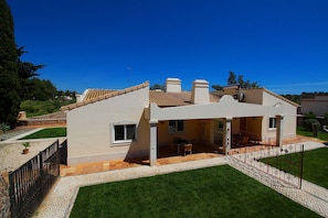 Una casa de dos pisos con un patio, una zona de estar al aire libre techada y un jardín pequeño.