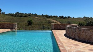 Piscina con paredes de piedra y vistas a viñedos bajo un cielo despejado.