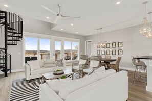 Un salon spacieux avec un canapé blanc, un coin repas avec des chaises en osier et une cuisine avec un bar.