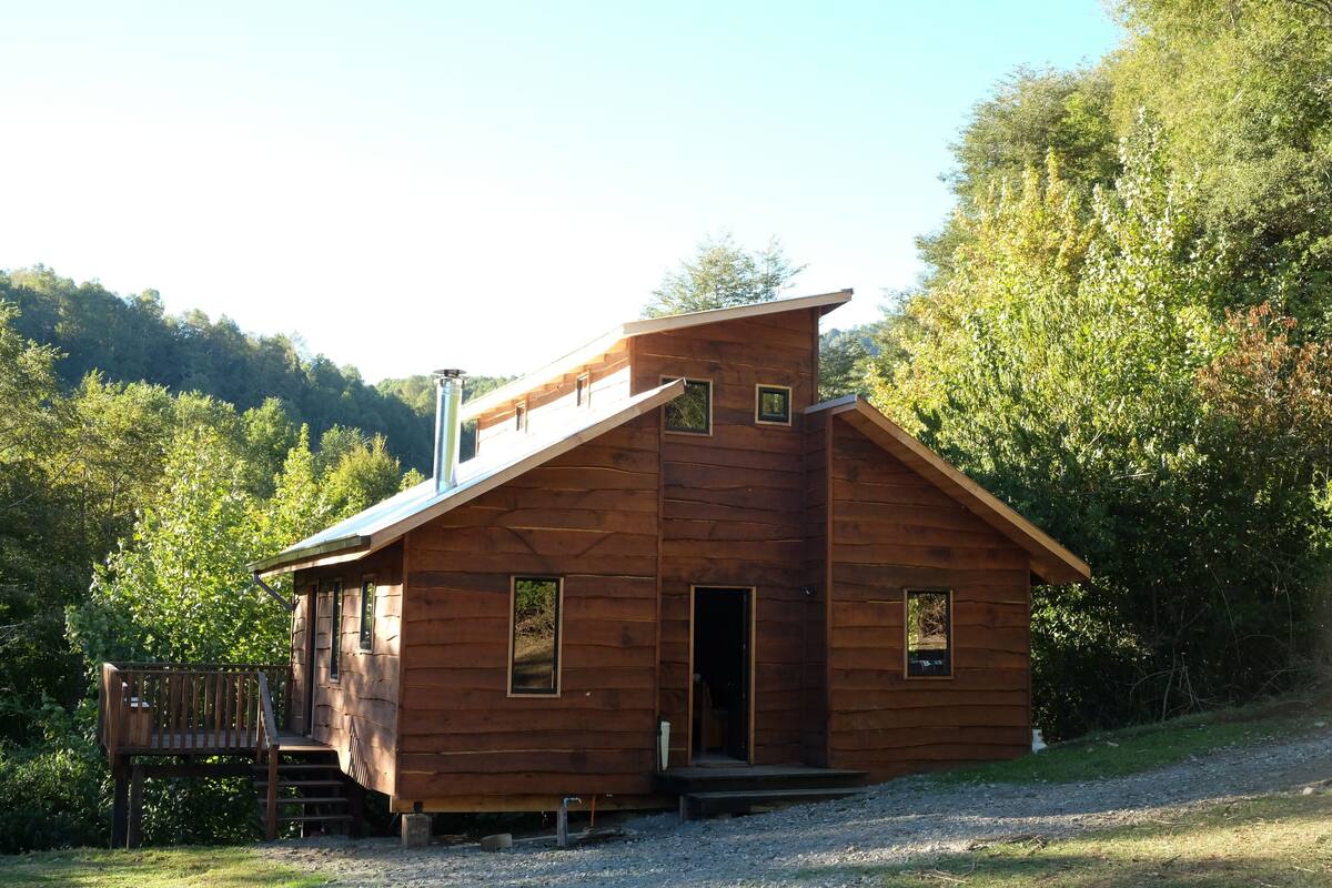 Een houten chalet met een schuin dak, een klein terras en een grindpad.
