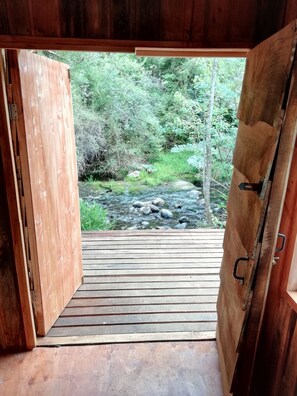 Une porte en bois ouverte donne sur une terrasse en bois, d’où l’on peut admirer un ruisseau et une forêt.
