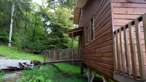 Une cabane en bois dotée d’une terrasse en bois et d’un petit pont menant à un porche.