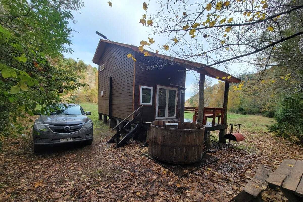Een chalet met een overdekte veranda, een hottub en een auto in de buurt.