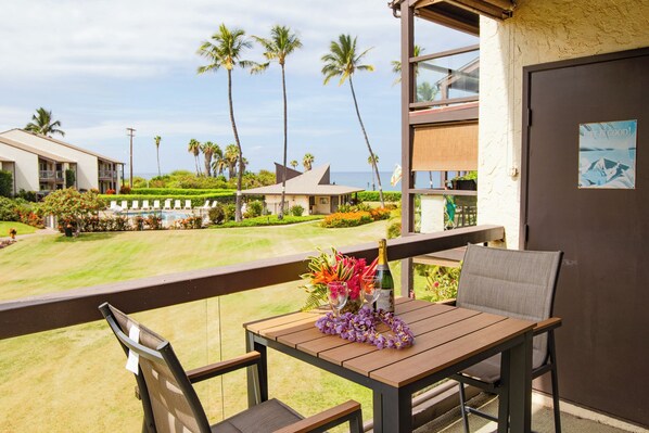A balcony with a table and chairs, overlooking a pool and palm trees.