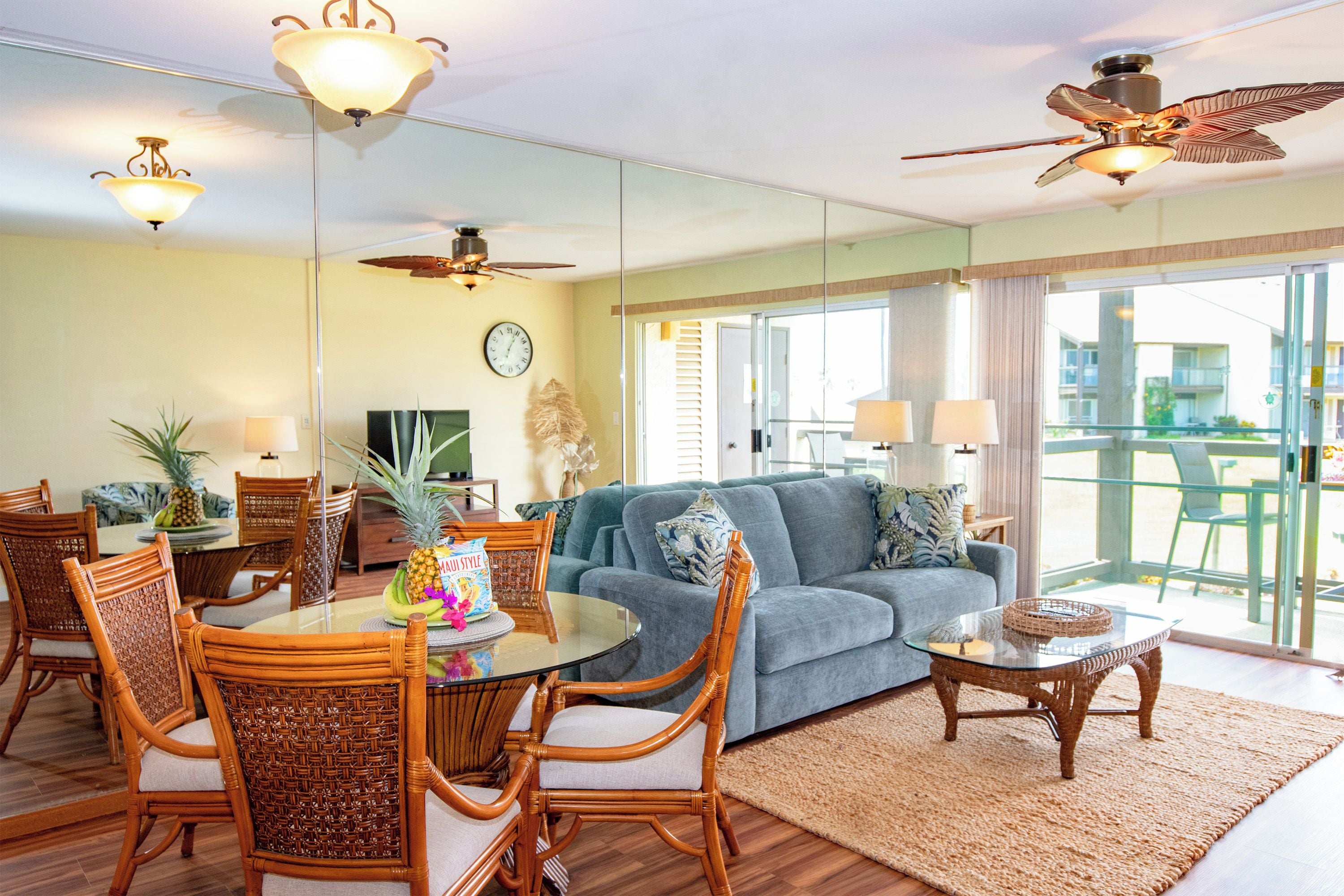 A spacious living area with a dining table, wicker chairs, a blue sofa, and a ceiling fan.
