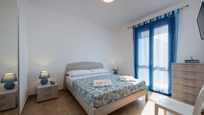 A bedroom with a bed, two bedside tables, a dresser, and a chair. - I Tre Golfi Ghaliya Apartment (San Vito Lo Capo)