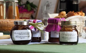 Three jars of preserved fruits and vegetables on a table with a loaf of bread and pastries in the background. - Room with a convivial spirit in the Vatican area (Roma)