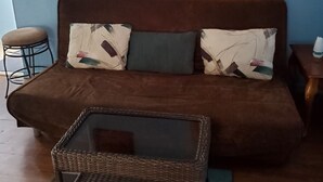 A cozy living room with a brown sofa, two patterned cushions, a wicker coffee table, a blue wall, and a decorative poster.