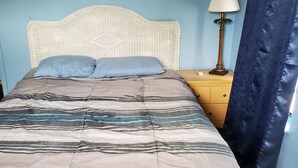 A bed with a striped bedspread, a nightstand with a lamp, and a wall with a cityscape painting.