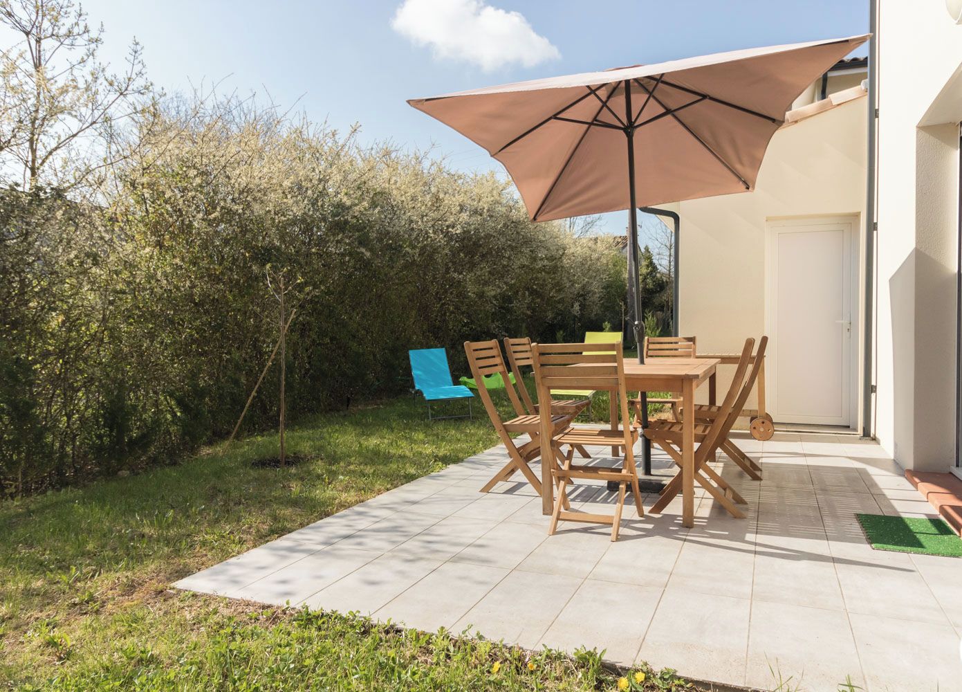 An outdoor patio with a table and chairs, a large umbrella, and a green chair.