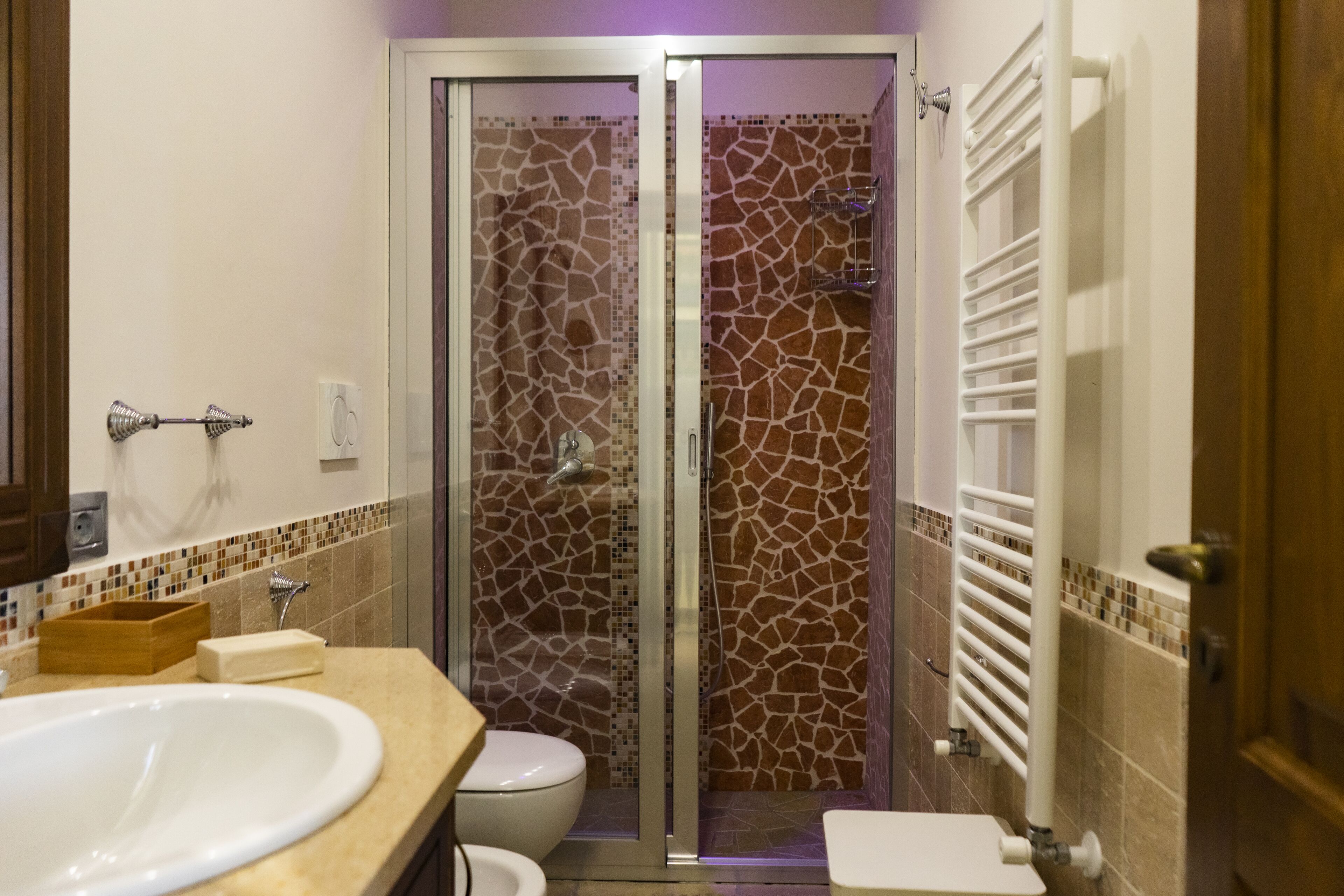 A bathroom with a white sink, toilet, and a shower enclosure with a mosaic wall.