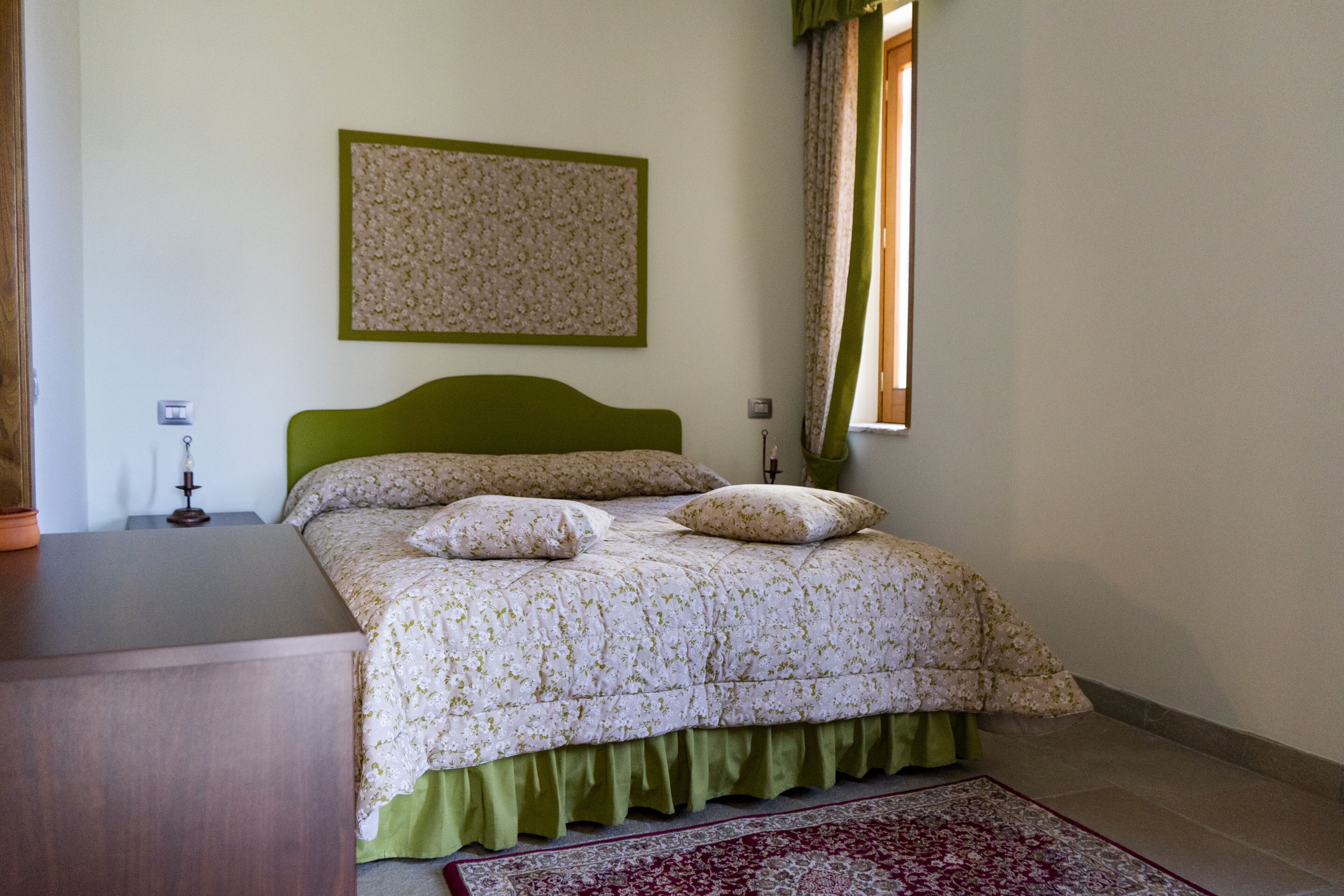 Une chambre à coucher comprenant un lit, une table de chevet, une lampe fixée au mur et un tableau orné de motifs floraux.