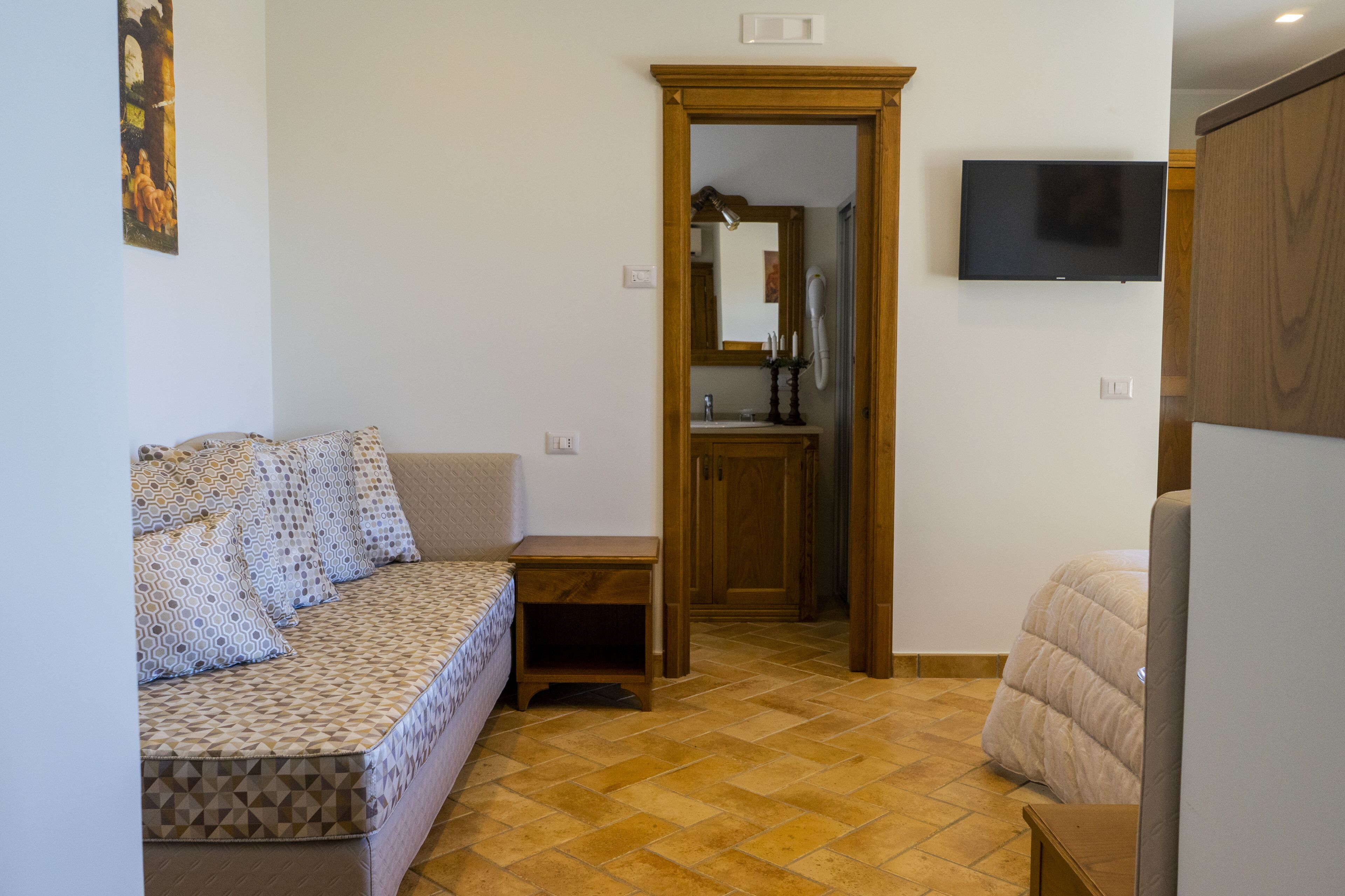 A room with a sofa, a small table, a wooden door leading to a bathroom, and a mounted TV.
