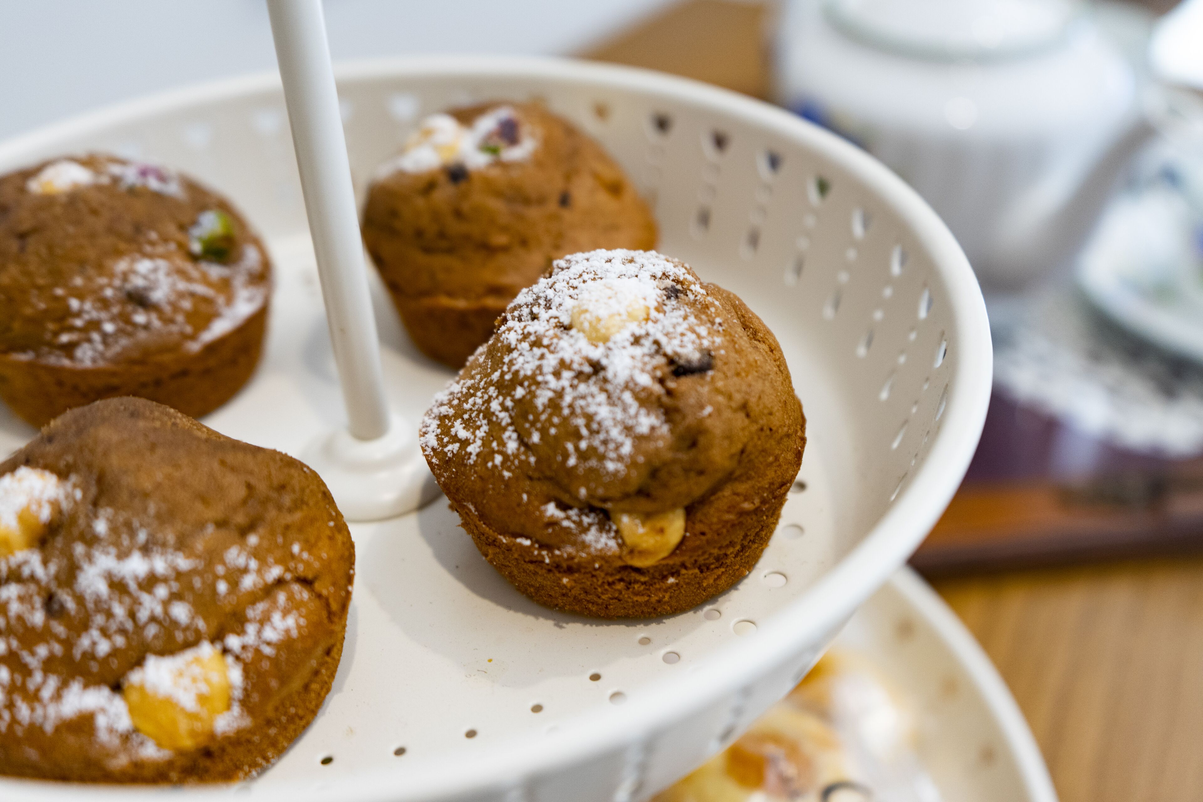 Un colador blanco con tres muffins, uno de ellos espolvoreado con azúcar glas.
