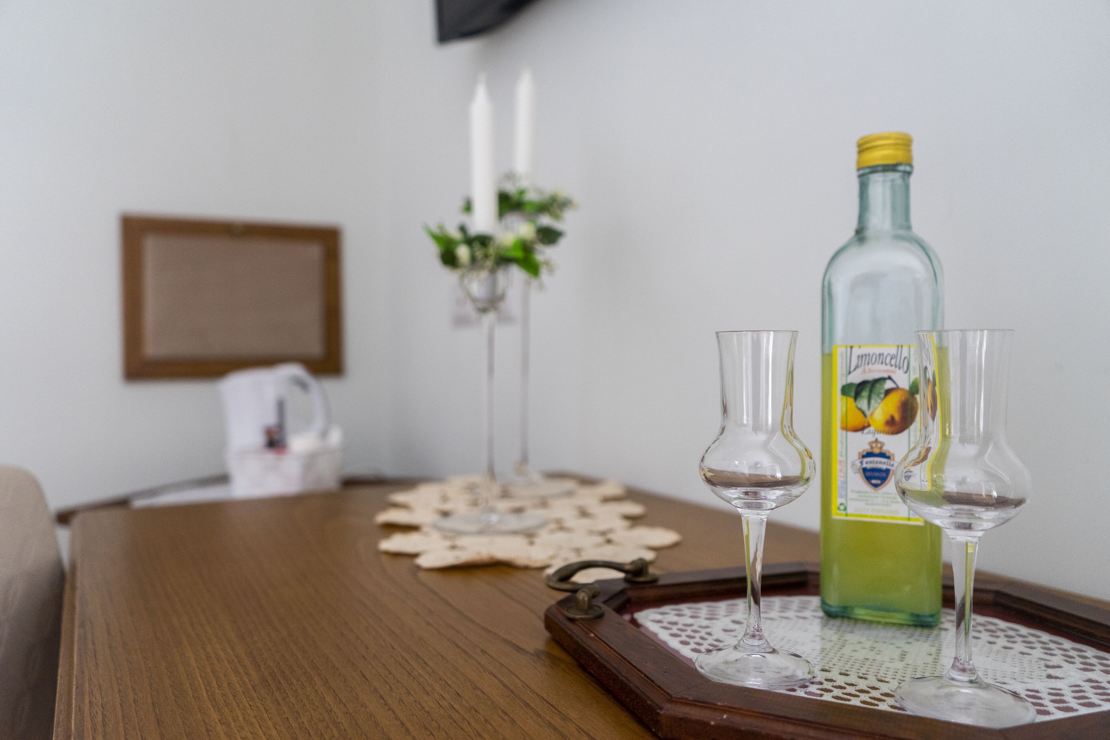 A wooden table with a bottle of Limoncello and two glasses on a tray.