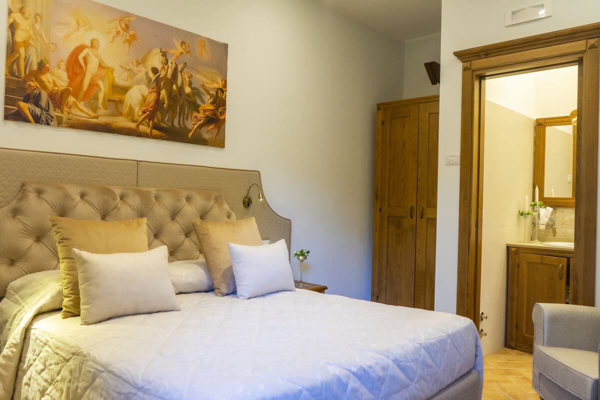 Quarto com uma cama grande, cabeceira, guarda-roupa de madeira e um quadro na parede.