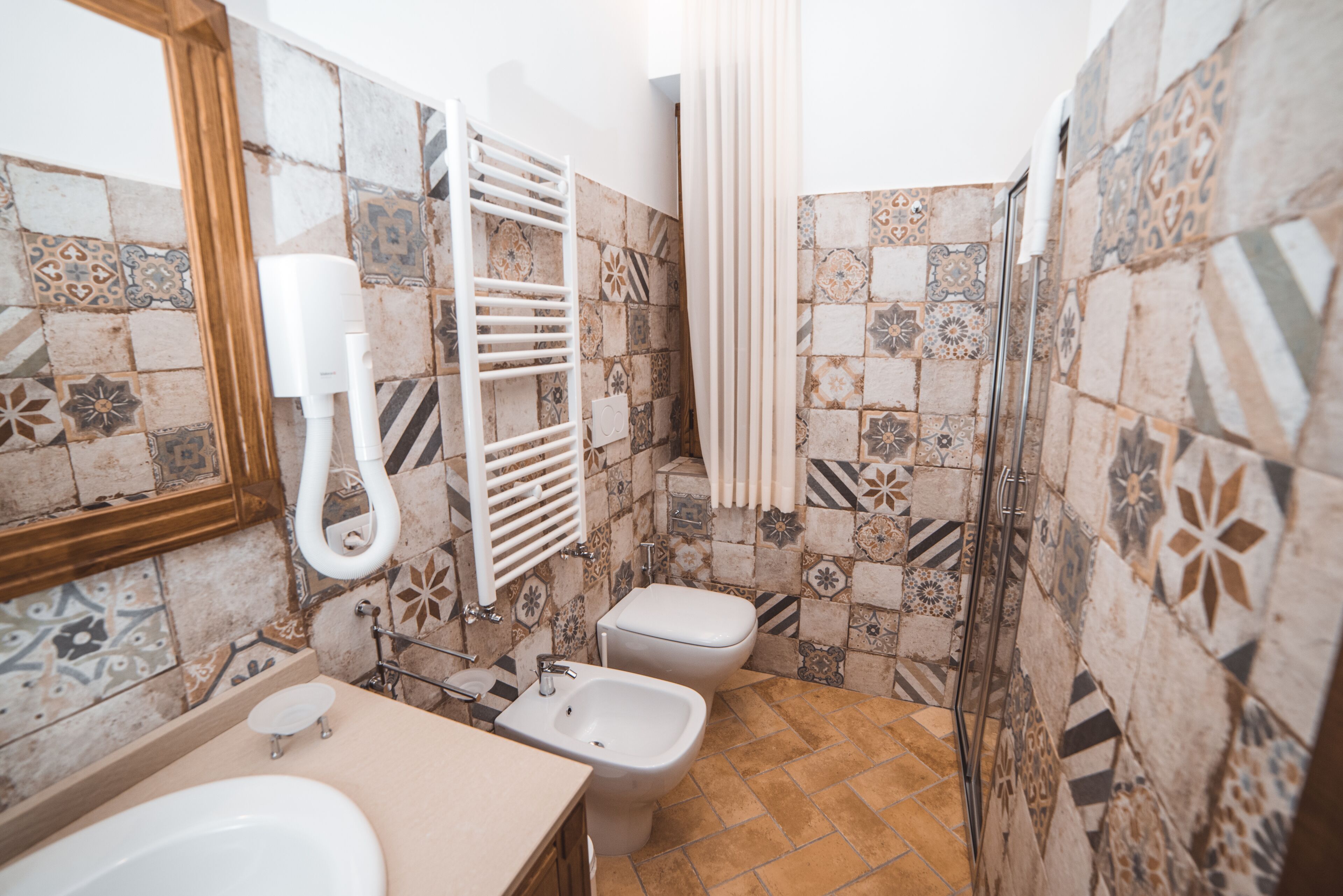 Un baño con ducha, dos inodoros, un lavamanos y un perchero para toallas.