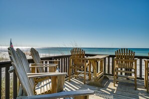 Une terrasse en bois avec des fauteuils Adirondack et une table, le tout offrant une vue sur la plage.