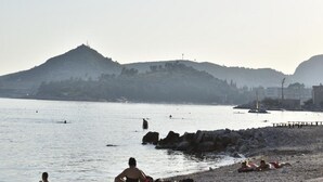 Una playa con costa rocosa, agua tranquila y colinas al fondo.