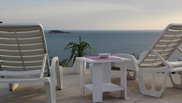 Una terraza frente al mar con dos sillones blancos, una mesita y una planta en maceta.