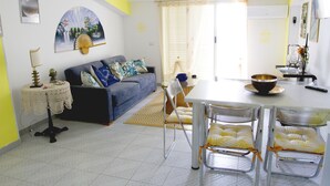 Una sala de estar con un sofá, una mesa de comedor con sillas, una mesa auxiliar y un abanico decorativo.