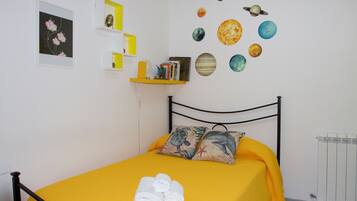 A bedroom with a bed, pillows, a yellow bedspread, a wall with a celestial-themed decoration, a shelf with books, and a framed picture.