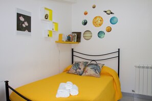 Ein Schlafzimmer mit einem Bett, Kissen, einer gelben Bettdecke, einer Wand mit himmelsthematischer Dekoration, einem Regal mit Büchern und einem gerahmten Bild.