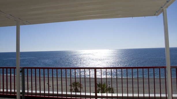 Vista a la playa desde un área techada con barandilla.