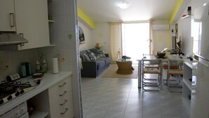 Una cocina compacta con estufa a gas, armarios blancos y una zona de comedor con sillas metálicas.