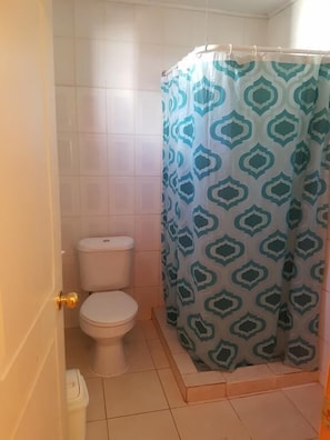 A bathroom with a toilet, a shower curtain with a geometric pattern, and a tiled floor.