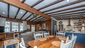 Uma sala de estar ampla com uma mesa de jantar de madeira, cadeiras brancas e um sofá cinza grande.