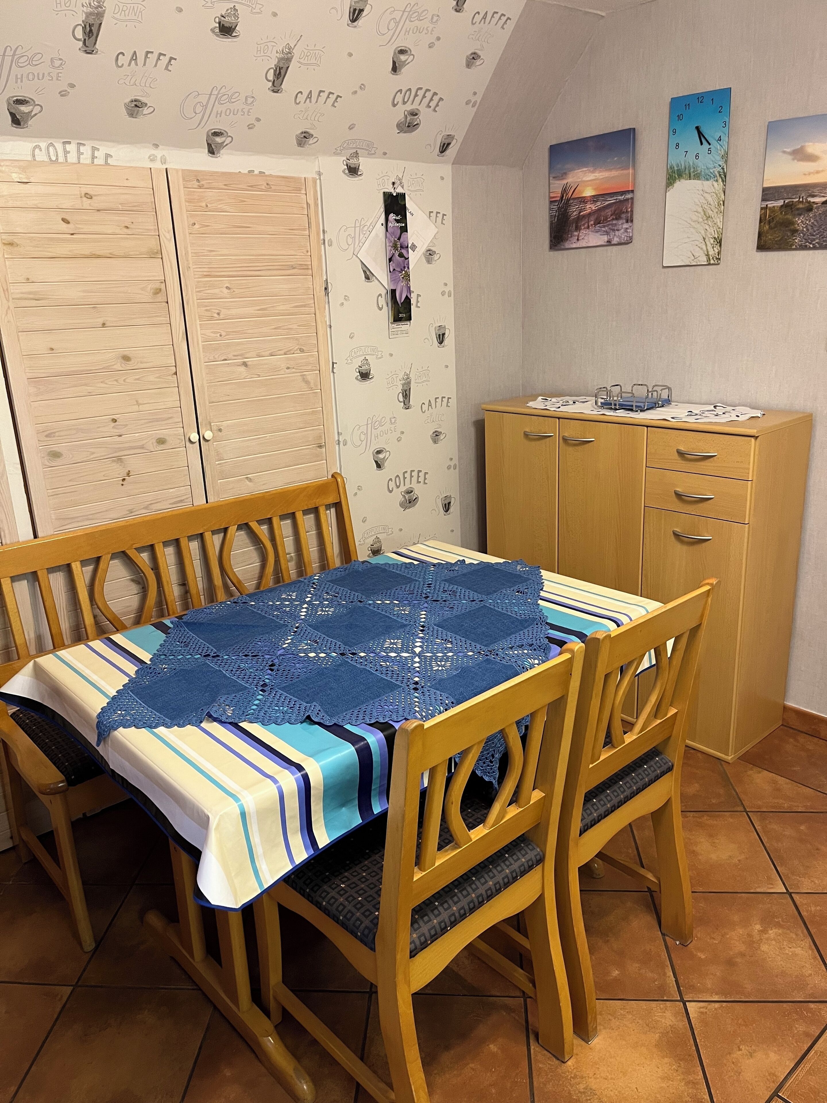 A dining area with a wooden table and chairs, a blue table runner, and a cabinet with drawers.