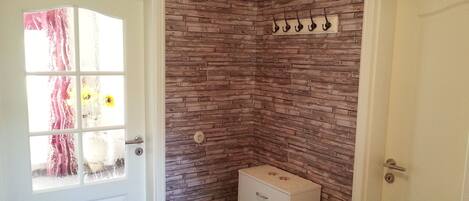 A room with a white door, a window with a curtain, a brick-patterned wall, and a small white cabinet.