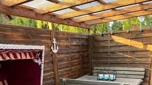 Une terrasse extérieure accueillante, avec un banc en bois, un coin salon confortable doté d’un coussin à rayures et une table sur laquelle est posé un chandelier.